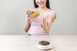 © KMPZZZ - Diet, dieting, happy asian young woman, girl hand push out, deny sweet donut, doughnut on plate, choose green vegetable salad bowl, eat food for good healthy, female getting weight loss.