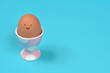 © nahhan - A brown chicken egg with a simple drawn happy face sits in a pink and white polka dot ceramic cup on a blue background