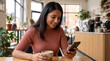 © OlgaNeuroArt - Young woman using smartphone in a modern cafe. Smiling female holding coffee cup while looking at mobile phone. Digital lifestyle and social media concept