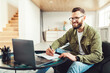 © Prostock-studio - Successful Businessman Using Laptop And Taking Notes Writing Schedule Or Doing Business Accounting Sitting In Chair At Home, Wearing Glasses. Happy Entrepreneur Or Freelancer Working Online