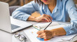 © kucherav - Woman analyzing financial report and writing notes on paper charts beside laptop. Business planning, data analysis, strategy, accounting, productivity, home office