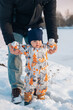 © phpetrunina14 - Baby in Snowsuit Held by Adult in Snowy Landscape.