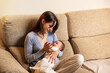 © Ametz - Mother bottle feeding newborn baby on sofa at home