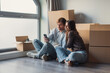 © Daniel - A happy couple embraces among cardboard boxes in a new home, laughing and celebrating their move while checking services on a smartphone during the relocation process