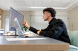 © Wavebreak Media - Asian man wearing glasses analyzing data on monitor, laptop beside coffee cup at office, copy space