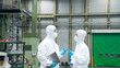 © metamorworks - 防護服を着て工場の中で話す男女作業員