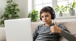 © MdNazim - Boy wearing headphones sitting on couch with laptop giving thumbs up 1