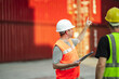© Wanwajee - Port terminal supervisor reviewing shipment checklist and directing logistics worker. Global trade and distribution management concept.