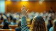 © Alex Alex - A student raises her hand in a crowded lecture hall, wanting to ask a question or answer one. Education concept, active participation, learning, seminar.