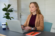 © Wavebreak Media - Woman in twenties wearing blazer working on laptop at office desk with coffee cup, copy space