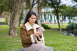 © leungchopan - Young woman using cellphone outside in park