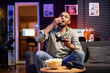 © DC Studio - Male gamer eating popcorn while he plays online shooting tournament, having fun with video games in his free time at home. Relaxed guy enjoying game night with snacks and competition.