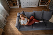 © Migma_Agency - Woman relaxing at home reading book on sofa