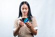 © Ryan - A young Asian woman in a beige vest holding and carefully looking at a variety of credit cards in her hands, isolated on a white studio background.