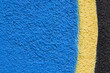 © nahhan - A close up shot of a rough textured wall painted with vibrant blue and yellow colors featuring a black border on the side