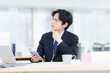 © gohan - オフィスでノートパソコンで仕事をする困った顔のスーツを着た若い日本人男性