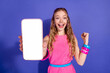 © deagreez - Cheerful young woman holding a smartphone with a blank screen against a vibrant purple background