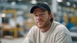 © VICHIZH - Young man wearing cap and casual sweatshirt looking at camera with confident expression in industrial warehouse environment with blurred background and soft lighting.