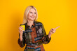 © deagreez - Elegant mature woman with blonde hair holding a yellow coffee cup smiles as she points to the right against a bright yellow background