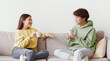 © Prostock-studio - Young Asian man and woman drinking coffee and talking while sitting on couch at home. Loving millennial couple enjoying coffee while having conversation, spending weekend together
