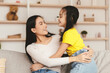 © Prostock-studio - Happy satisfied chinese young female look at girl have fun, hugging, enjoying time together in living room interior, copy space. Family spare time and weekend, love and people, relationships at home
