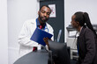© DC Studio - Black physician in lab coat and receptionist read through updated healthcare data to ensure accuracy. Clinic administrator listens to doctor with clipboard, receiving lists of completed appointments