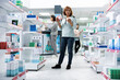 © DC Studio - Asian female customer holds medical product boxes, carefully reading labels in pharmacy aisle. Browsing indoor shelves, woman demonstrates informed healthcare decisions and consumer curiosity.