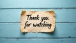 © miss irine - Torn paper note with handwritten phrase thank you for watching rests on weathered blue wood planks. Simple background for video end screens presentations or social media content.