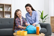 © New Africa - Mother and daughter packing backpack for school on sofa at home