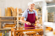 © JackF - Elderly salesman works in sales area of bakery, stands near counter and packs croissant in transparent disposable plastic bag.