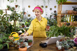 © sofiko14 - A woman in a yellow shirt holds a potted succulent in a plant shop, surrounded by greenery and other plants