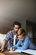 © peopleimages.com - Writing, child or dad with homework support in home for education, development or academic growth. Learning, father or boy with book at table for study lesson, exam preparation or guidance with space