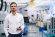 © Westend61 - Confident young businessman holding digital tablet while standing at illuminated factory