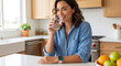 © Atmospheres - Happy woman drinking water in kitchen wearing smartwatch for hydration and healthy lifestyle