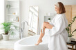 © Pixel-Shot - Young woman massaging her leg with brush on bathtub at home