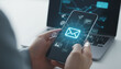 © Md - Smartphone user holding mobile device showing glowing email icon and digital communication network symbols with laptop in background during daytime