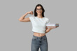 © Pixel-Shot - Young woman in eyeglasses holding books and flexing muscles on grey background. Feminism concept