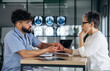 © standret - Male healthcare professional in blue scrubs discusses medical results with female patient in a modern clinic setting, medical imaging displayed in the background