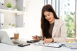 © Fahng - Successful business woman economist in formal wear using calculator, sitting at her work place in  office, working on laptop making report.