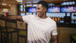 © Krakenimages.com - Man smiling and pointing with outstretched arm toward bar tv screens in a lively sports bar wearing a light pink t shirt; joy socializing.