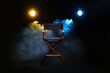 © New Africa - Film director's chair and lighting equipment on black background with smoke