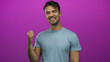 © Krakenimages.com - Young hispanic man smiling confidently with his thumb pointed over shoulder against an isolated pink background, wearing a casual blue t-shirt, embracing a positive mood.