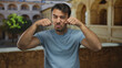 © Krakenimages.com - Young hispanic man making a playful crying gesture in front of an old university courtyard, capturing a humorous outdoor moment.