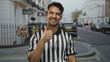 © Krakenimages.com - Young hispanic man referee on a city street gives a thumbs-up, showcasing positivity in an outdoor urban setting.