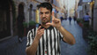 © Krakenimages.com - Young hispanic man in referee uniform making loser gesture on a street in a city, capturing attention with a playful expression and urban backdrop.