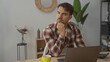 © Krakenimages.com - Young man in plaid shirt focused on laptop at desk in modern office surrounded by plants and books displaying concentration and work environment