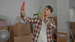 © Krakenimages.com - Young man taking selfie in new apartment surrounded by moving boxes with indoor plants and casual attire.