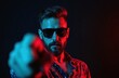 © Maryna - Man with sunglasses points finger at camera. Neon blue and red light illuminates dark studio background. Focused guy shows direction gesture. Direct gaze, confident expression, stylish man.