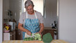 © luciano - Elderly woman wearing apron chops fresh broccoli on a kitchen counter. The close-up scene highlights healthy meal preparation, emphasizing fresh vegetables, home cooking