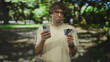 © Krakenimages.com - Man holds smartphone and creditcard, frowning while checking phone in studio, hands raised slightly with bracelets and round glasses visible; frustration.
